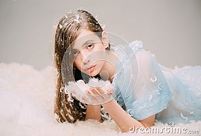 Lovely girl with long brunette hair holding handful of tiny feathers. Cute female teenager in blue lace nightgown lying Stock Photo