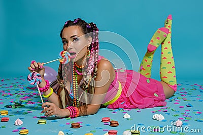 Lovely girl with a multi-colored braids hairstyle and bright make-up, posing in studio with lollipop, air balloons and Stock Photo