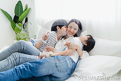 Lovely happy Asian family at cozy home. Son and daughter kiss mother with enjoy ,relax and playful together in bedroom. Happiness Stock Photo