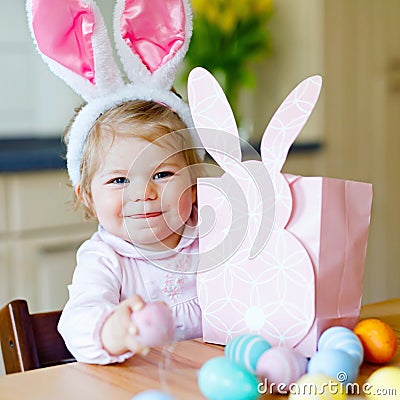 Lovely little toddler girl wearing Easter bunny ears playing with colored pastel eggs. Happy baby child unpacking gifts Stock Photo