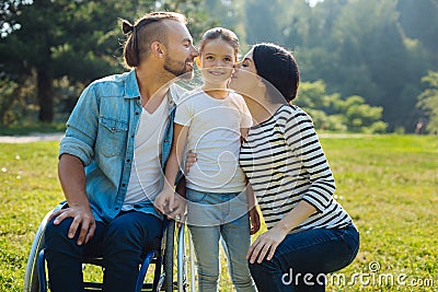 Lovely mother and father kissing their daughter on cheeks Stock Photo