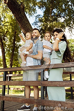 Lovely parents with little kids at the park, beautiful mother hold in arms joyful son, cute daughter sitting in fathers Stock Photo