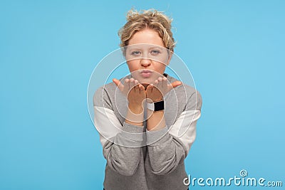Lovely sensual woman with short curly hair in casual sweatshirt sending air kiss to camera, expressing affection and fondness Stock Photo