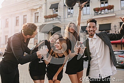 Lovely tanned lady with helium balloons dancing on the street near african friend. Outdoor portrait of young people Stock Photo