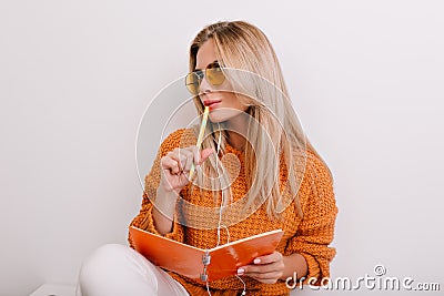 Lovely white woman writing poetry in colorful notebook and thinking about rhymes. Pensive fair-haired girl holding pen Stock Photo