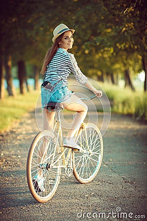 Lovely young woman in a hat riding a bicycle in a park Stock Photo