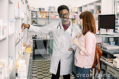 Lovely young woman smiling, buying medicines at the drugstore. African man pharmacist helping his female customer Stock Photo