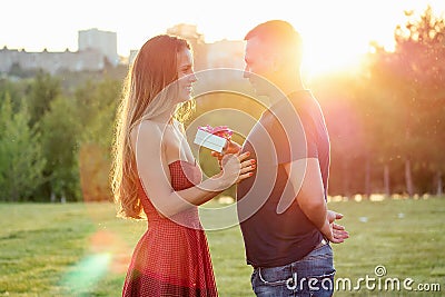 Lover boyfriend gives a gift box to embarrassed attractive beautiful blonde long hair bride in love in evening cocktail Stock Photo