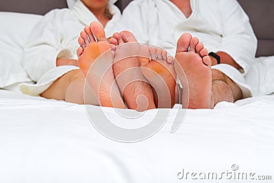 Lovers feet of a couple in love in a bed with white linens Stock Photo
