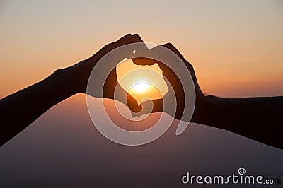 Lovers hands in heart shape with sunset background Stock Photo