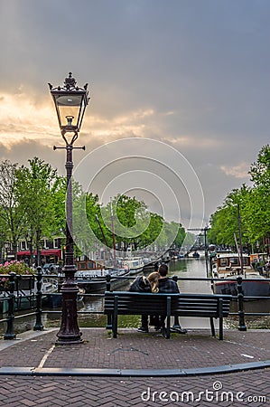 Lovers sit together at twilight overlooking a canal in Amsterdam Editorial Stock Photo