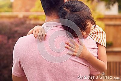 Loving Asian Father Cuddling Daughter In Garden As Girl Looks Over His Shoulder Stock Photo
