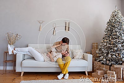 Loving, cheerful couple on a sofa near Christmas tree with gifts sits on a white sofa. Crazy lovers Stock Photo