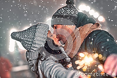A loving couple dressed in knitted hats and scarves celebrate the New Year against the backdrop of the night city, hold sparklers Stock Photo