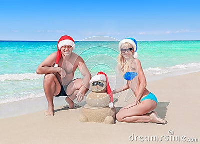 Loving couple and funny sandy Christmas snowman in santa hats at sea beach Stock Photo