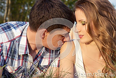 Loving couple of guys and girls lying on the grass on the meadow, man kissing a girl on the shoulder Stock Photo