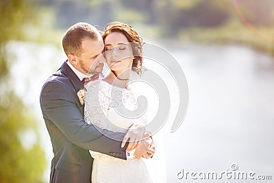 Loving couple of newlyweds walks near wide river in summer sunny day Stock Photo