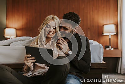 Loving couple sitting on the floor in bedroom and using tablet Stock Photo