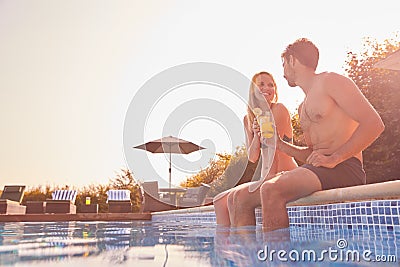 Loving Couple On Summer Vacation Sitting On Edge Of Swimming Pool With Cold Drinks Stock Photo