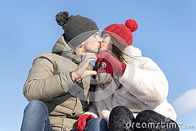 Loving couple in winter hats kissing against the blue sky and keeps hands in heart shape sign Stock Photo