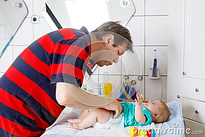 Loving father changing diaper of his newborn baby daughter. Little child, girl on changing table in bathroom with rattle Stock Photo