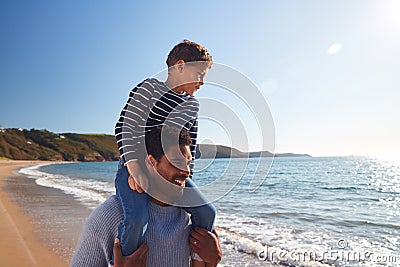 Loving Father Giving Son Ride On Shoulders As They Walk Along Beach Together Stock Photo