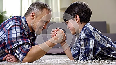 Loving father and kid arm wrestling on the floor, weekend leisure at home, fun Stock Photo