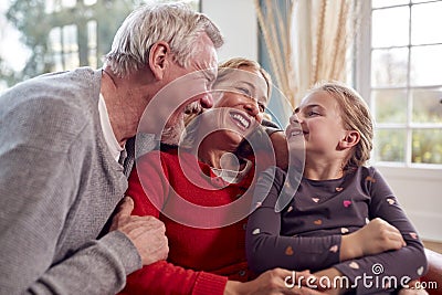 Loving Grandparents Hugging Granddaughter Sitting On Sofa At Home Together Stock Photo