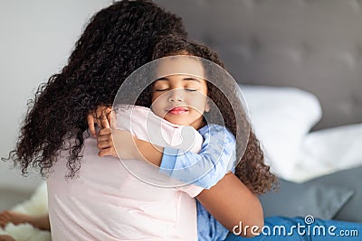 Loving little black girl in casual wear hugging her mother on bed at home. Strong family relationships concept Stock Photo