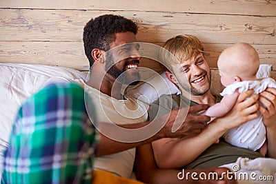 Loving Male Same Sex Couple Cuddling Baby Daughter In Bedroom At Home Together Stock Photo