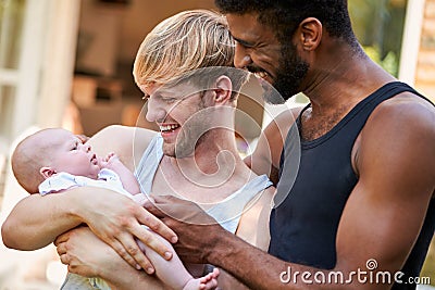 Loving Male Same Sex Couple Cuddling Baby Daughter At Home In Garden Together Stock Photo