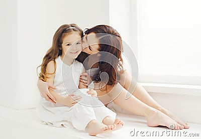 Loving mother kissing daughter at home in white room Stock Photo