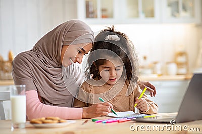 Loving Muslim Mom In Hijab Drawing With Her Little Daughter In Kitchen Stock Photo