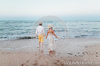 A boy and a girl stand on the beach with their backs and hold hands. Romantic story on the seafront. Stock Photo