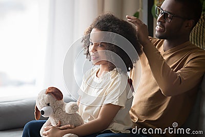 Loving black dad brush daughter hair sitting on couch Stock Photo