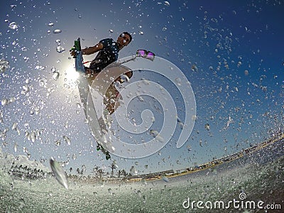 LOW ANGLE: Athletic young man splashes water at the camera while kitesurfing. Stock Photo