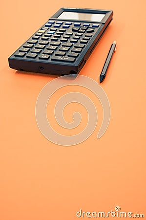 Low angle closeup of a graphing calculator and a tiny pen isolated on an orange background Stock Photo
