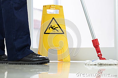 Low angle closeup of a person cleaning the floor with a mop near a yellow caution wet floor sign Stock Photo