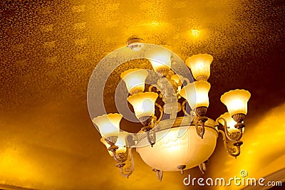 Low-angle of a luxurious vintage chandelier hanging on a ceiling, with many lightbulbs turned on Stock Photo