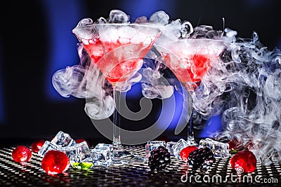 Low angle modern view dessert show or glass of red cocktail and smoke or dry ice steam, ice cubes blackberrys raspberries mint on Stock Photo