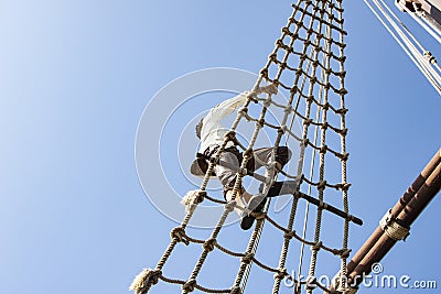 Low angle shot of a young sailor climbing by side rope ladders of a sailboat Stock Photo