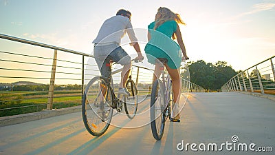 LOW ANGLE: Unrecognizable couple riding their bikes across an overpass at sunset Stock Photo