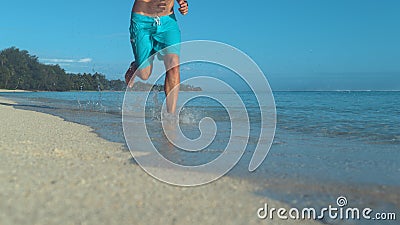 LOW ANGLE: Unrecognizable man runs barefoot down beautiful white sand beach. Stock Photo