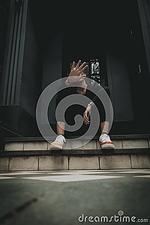 A vertical shot of a young hipster female raised her hand for dissuade while sitting on stairs Stock Photo