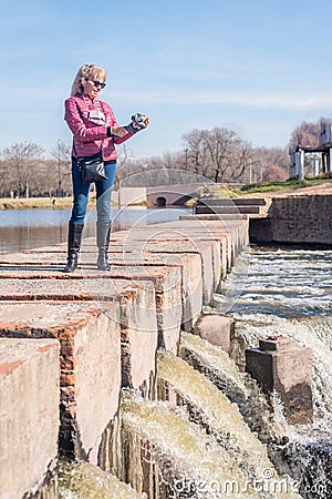 Low angle view of an adult woman standing on a brick walkway in the park holding a gimbal with phone Stock Photo