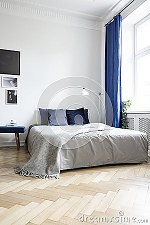 Low angle view of a cozy double bed in a corner of a bright bedroom interior with navy blue textiles and parquet floor Stock Photo