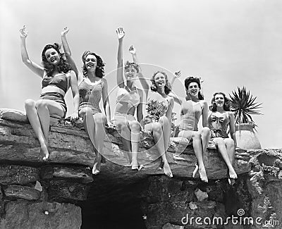 Low angle view of a group of women sitting on a stone structure and waving their hands Stock Photo