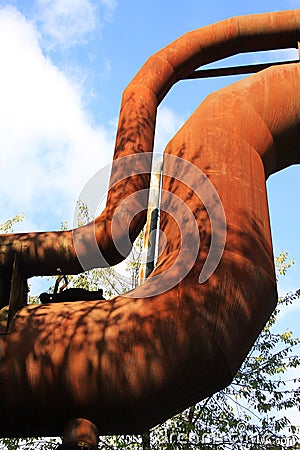 Landschaftspark Duisburg, Germany: Low angle view on isolated curved corroded pipeline against blue sky and trees Editorial Stock Photo