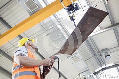 Low angle view of manual worker operating crane lifting sheet metal in industry Stock Photo