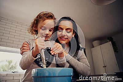 Low angle view of mother and daughter whisking batter in bowl and adding seasoning in bowl while cooking in kitchen Stock Photo